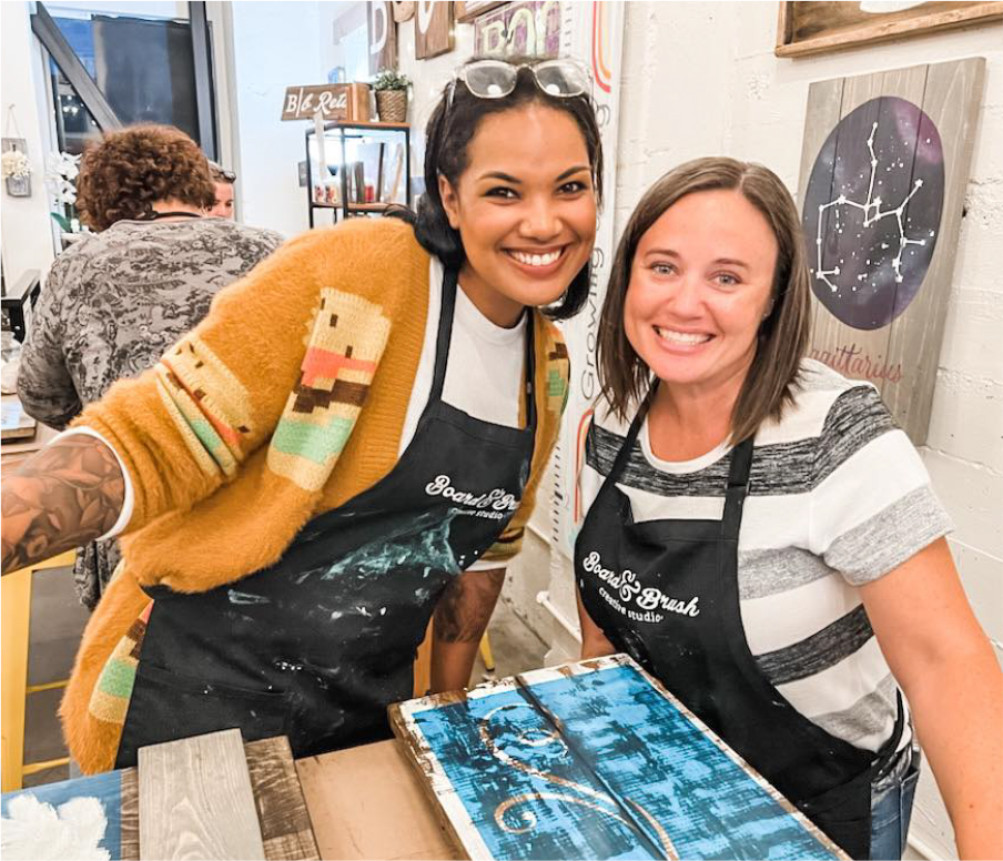 Two guests at a Board & Brush workshop in front of their completed projects